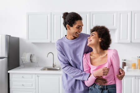 Young african american couple looking at each other while hugging in kitchen