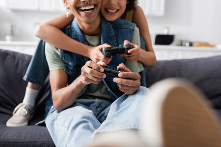 KYIV, UKRAINE - NOVEMBER 9, 2021: Cropped view of smiling african american couple playing video game...