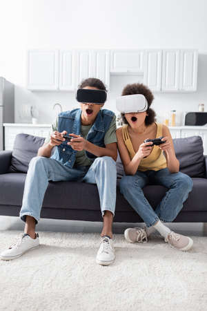 KYIV, UKRAINE - NOVEMBER 9, 2021: Shocked african american couple in vr headsets playing video game...