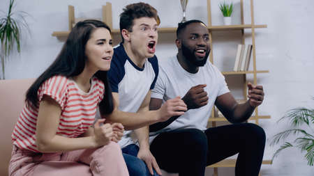 excited man screaming near happy interracial friends watching sport competition on tv