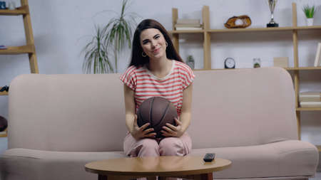 pleased woman sitting on sofa with ball while watching sport championship on home tvの写真素材