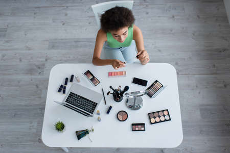 Overhead view of african american woman holding lip balm near devices and cosmetics on tableの写真素材