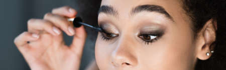 Cropped view of african american woman applying mascara at home, banner