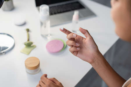 Cropped view of african american woman holding cosmetic cream near blurred laptop and jade roller on tableの写真素材