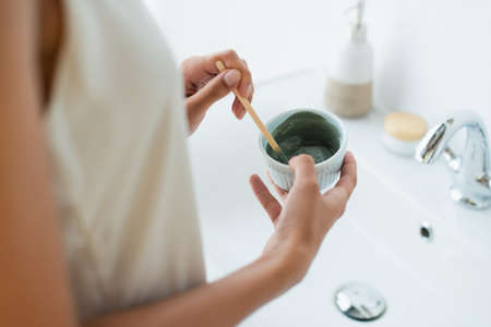Cropped view of african american woman in nightgown mixing face mask in bathroomの写真素材