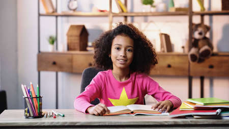 smiling african american child reading book and looking at camera
