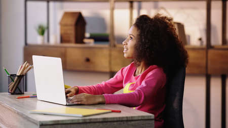 pleased african american child looking away near laptop