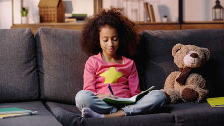 curly african american child doing homework on sofaの写真素材
