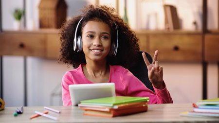 happy african american girl in headphones showing peace sign and holding digital tabletの写真素材
