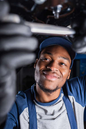 Smiling african american foreman working under car in service