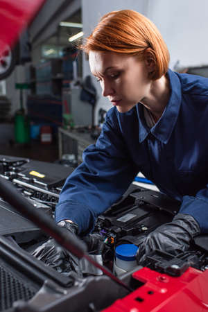 forewoman in uniform fixing motor of car in workshopの写真素材