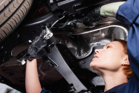 Low angle view of mechanic working with wrench and car in garageの写真素材