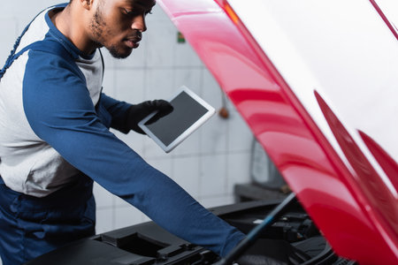 young african american repairman holding digital tablet with blank screen while inspecting carの写真素材
