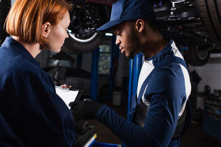 African american mechanic pointing at clipboard near colleague in car serviceの写真素材