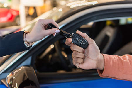 partial view of car dealer giving key to african american client near blurred car