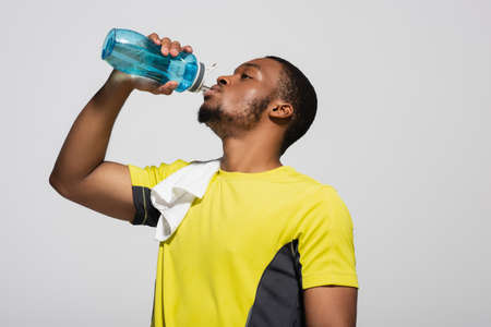 african american sportsman drinking water from sports bottle isolated on grey