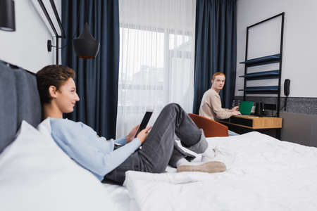 Young man using laptop near blurred girlfriend with digital tablet in hotel roomの写真素材