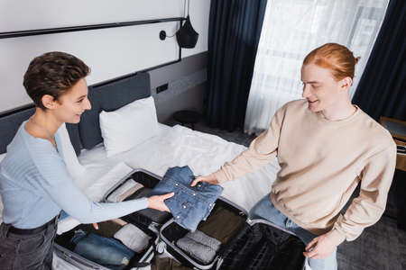 High angle view of smiling couple holding clothes near suitcases on bed in hotel roomの写真素材