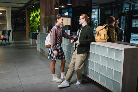 Side view of smiling tourists with backpacks talking near reception in hotelの写真素材