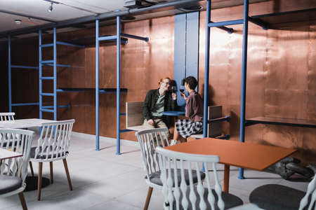 Positive man holding glass of wine near girlfriend in cafe in hotelの写真素材
