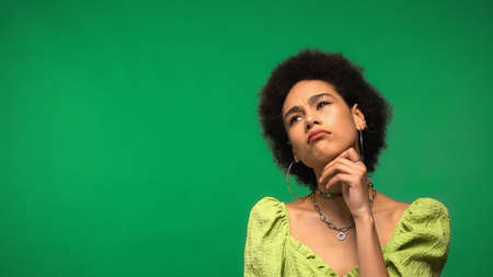 thoughtful african american woman in hoop earrings and blouse looking away isolated on greenの写真素材
