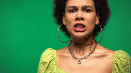 angry african american woman in hoop earrings isolated on greenの写真素材