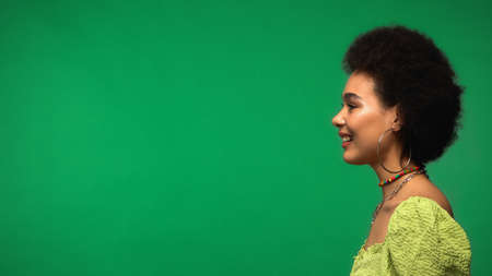 side view of cheerful african american woman smiling isolated on greenの写真素材