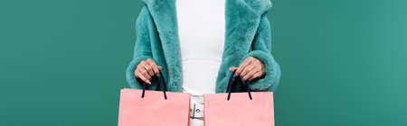 cropped view of woman in trendy faux fur jacket holding pink shopping bags isolated on green, bannerの写真素材