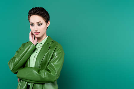 pretty woman in fashionable clothes holding hand near face while looking at camera on greenの写真素材