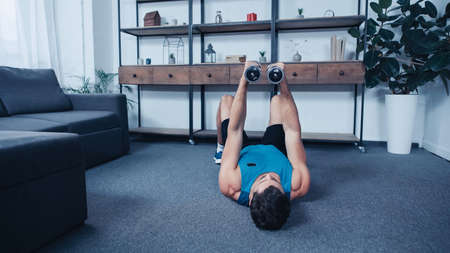 young sportsman lying on floor and training with dumbbells