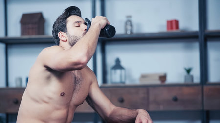 muscular sportsman holding sports bottle and drinking water at homeの写真素材