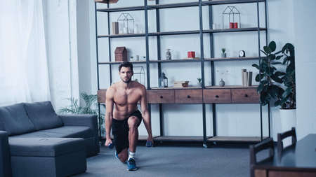 shirtless sportsman training with dumbbells at home