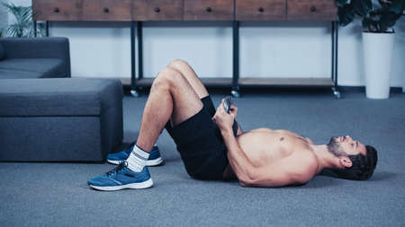 muscular sportsman working out with kettlebell on floor at home