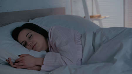 Brunette woman in pajamas sleeping on bed at home