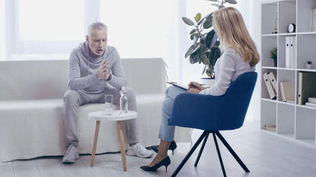 mature sportsman and blonde psychologist having conversation in consulting roomの写真素材