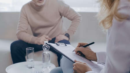 cropped view of psychotherapist writing in clipboard near mature patientの写真素材