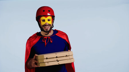 happy man in superhero costume holding boxes with pizza isolated on blueの写真素材