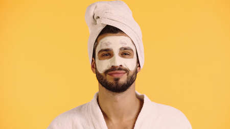pleased man with clay mask on face looking at camera isolated on yellowの写真素材