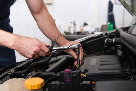 Cropped view of mechanic using wrench while working with auto in garage