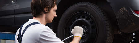 Side view of mechanic unscrewing car wheel in service, banner
