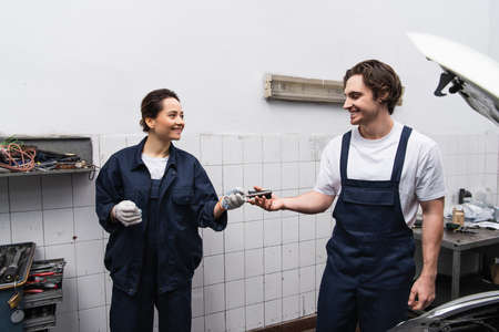 Smiling mechanics holding tool near car in service