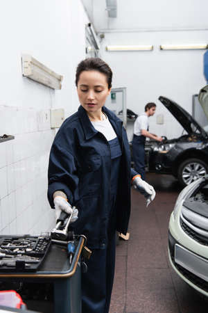 Young mechanic taking tool near auto and blurred colleague in garageの写真素材
