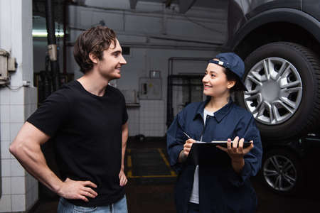 Positive driver standing near workwoman with clipboard near car in service