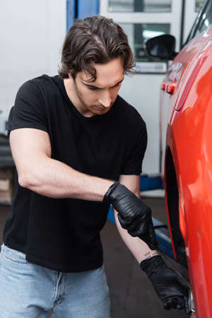 Workman in gloves working with screwdriver and car wheel in garageの写真素材