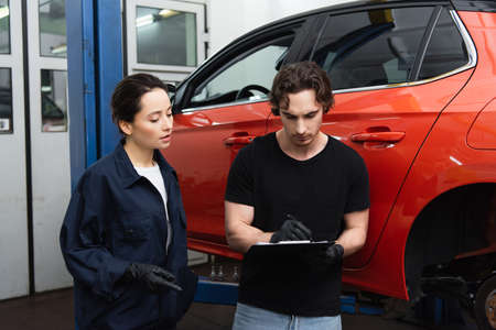 Mechanics in gloves writing on clipboard near auto in garageの写真素材