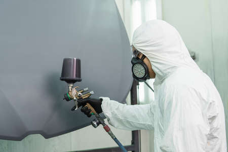 Side view of workman in respirator coloring car hood while working in service