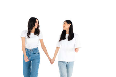 cheerful interracial women holding hands and looking at each other isolated on white