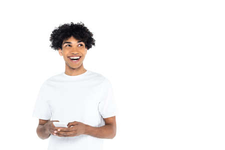 excited african american man looking away while messaging on smartphone isolated on whiteの写真素材