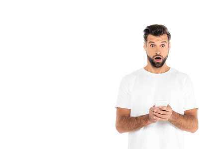 astonished man with open mouth messaging on mobile phone while looking at camera isolated on white