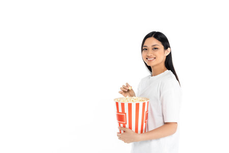 happy asian woman in t-shirt holding big bucket of popcorn isolated on whiteの写真素材